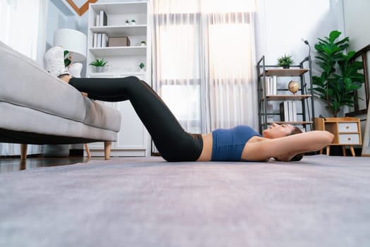 Young attractive asian woman in sportswear lies on the floor and doing sit-ups on the crouch, aiding targeting on abs muscle for effective home exercise routine. Vigorous
