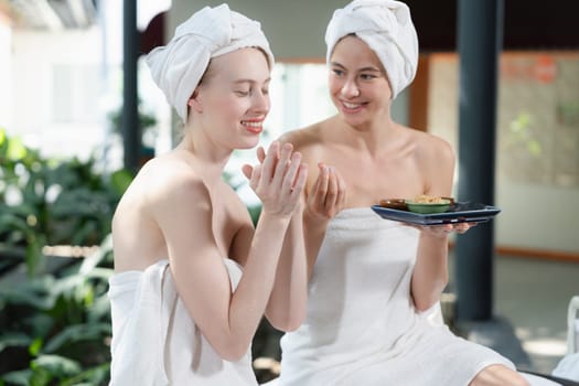 Portrait of two attractive woman in towel giggling during hold the herbal bowl surrounded by natural spa environment. Pretty girls with beautiful skin using herbal scrub at spa salon.Tranquility.