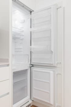 Photo of an open, empty and white refrigerator in a modern kitchen.