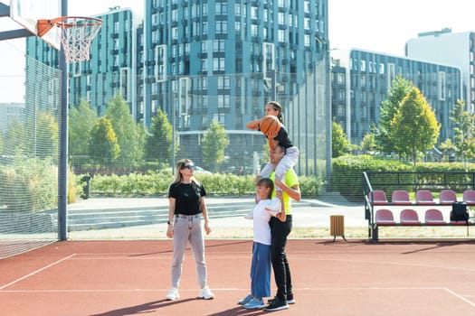 summer holidays, sport and people concept - happy family with ball playing on basketball playground. High quality photo