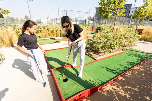 Mother and her little daughter practicing to hit the ball at the course. High quality photo