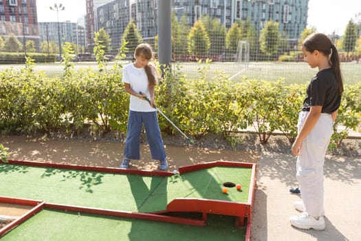 Cute school girl playing mini golf with family. Happy toddler child having fun with outdoor activity. Summer sport for children and adults, outdoors. Family vacations or resort. High quality photo