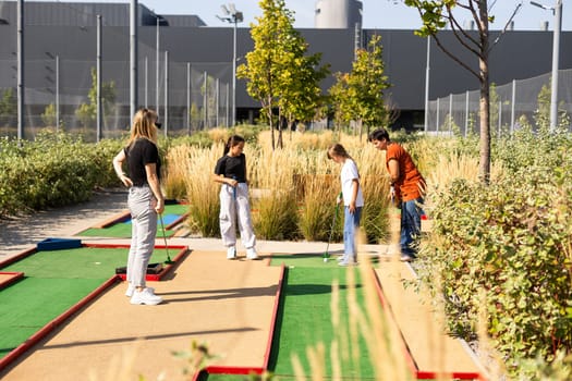 Group of smiling friends enjoying together playing mini golf in the city. High quality photo