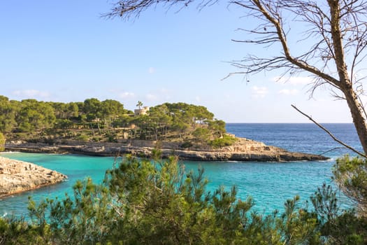 View of rocky shoreline with lush trees and calm blue sea, cala mondrago, mallorca, balearic island, spain,