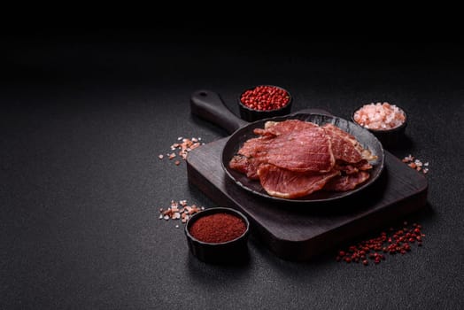Jerky, dried pork meat slices with salt and spices on a dark concrete background