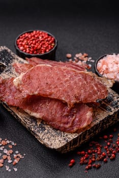 Jerky, dried pork meat slices with salt and spices on a dark concrete background