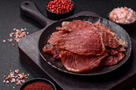 Jerky, dried pork meat slices with salt and spices on a dark concrete background