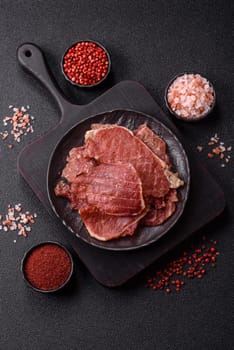 Jerky, dried pork meat slices with salt and spices on a dark concrete background
