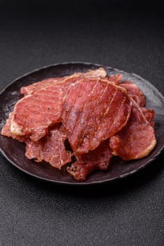 Jerky, dried pork meat slices with salt and spices on a dark concrete background