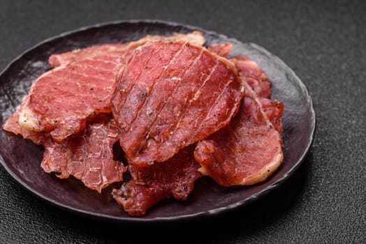 Jerky, dried pork meat slices with salt and spices on a dark concrete background