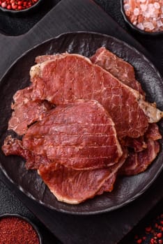 Jerky, dried pork meat slices with salt and spices on a dark concrete background