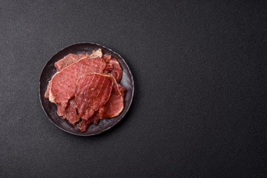 Jerky, dried pork meat slices with salt and spices on a dark concrete background