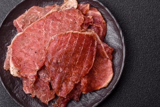 Jerky, dried pork meat slices with salt and spices on a dark concrete background