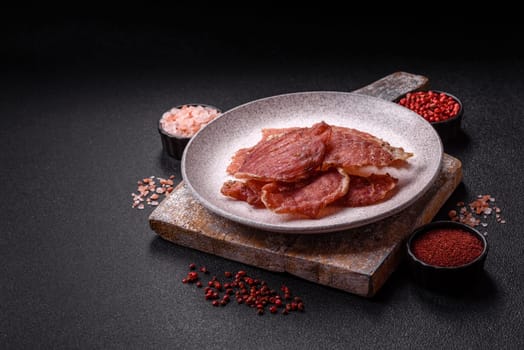 Jerky, dried pork meat slices with salt and spices on a dark concrete background