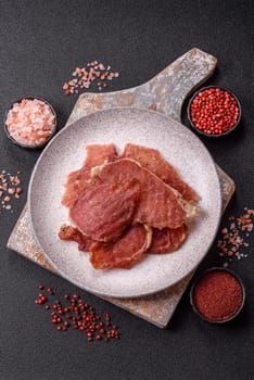 Jerky, dried pork meat slices with salt and spices on a dark concrete background