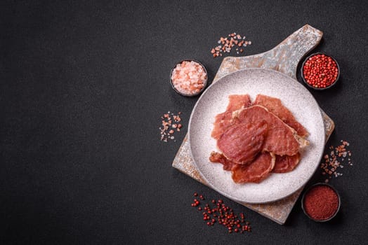 Jerky, dried pork meat slices with salt and spices on a dark concrete background