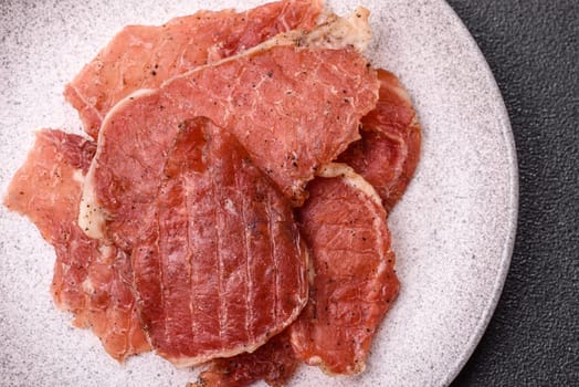Jerky, dried pork meat slices with salt and spices on a dark concrete background