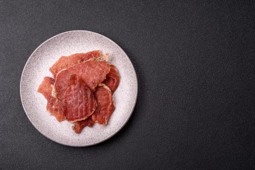 Jerky, dried pork meat slices with salt and spices on a dark concrete background