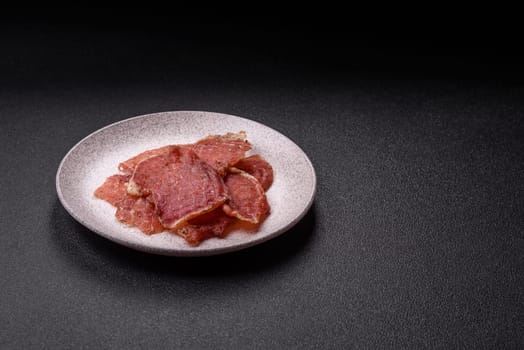 Jerky, dried pork meat slices with salt and spices on a dark concrete background