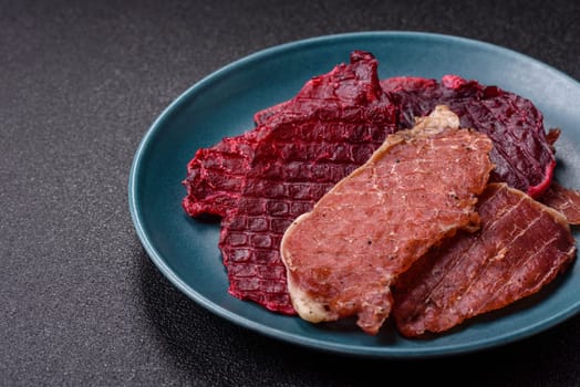 Jerky, dried pork meat slices with salt and spices on a dark concrete background