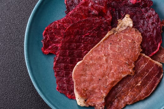 Jerky, dried pork meat slices with salt and spices on a dark concrete background