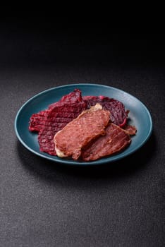 Jerky, dried pork meat slices with salt and spices on a dark concrete background
