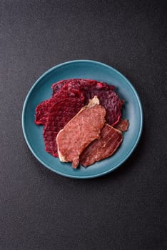 Jerky, dried pork meat slices with salt and spices on a dark concrete background