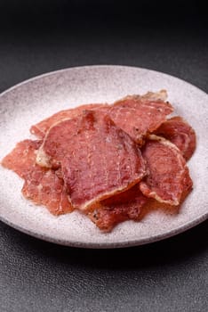 Jerky, dried pork meat slices with salt and spices on a dark concrete background