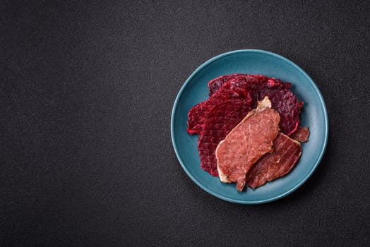 Jerky, dried pork meat slices with salt and spices on a dark concrete background