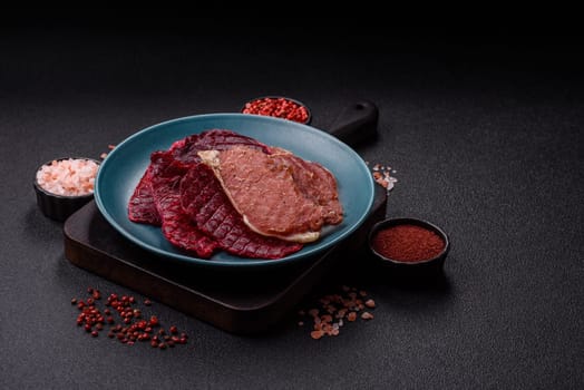 Jerky, dried pork meat slices with salt and spices on a dark concrete background