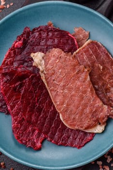 Jerky, dried pork meat slices with salt and spices on a dark concrete background