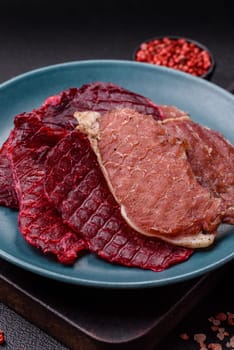 Jerky, dried pork meat slices with salt and spices on a dark concrete background