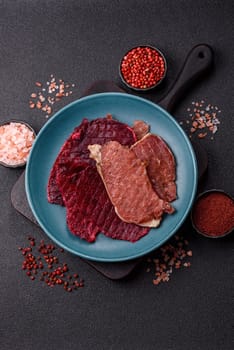 Jerky, dried pork meat slices with salt and spices on a dark concrete background