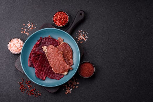 Jerky, dried pork meat slices with salt and spices on a dark concrete background