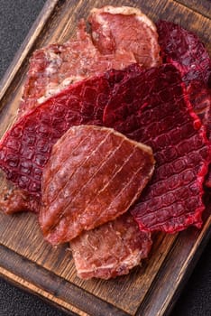 Jerky, dried pork meat slices with salt and spices on a dark concrete background