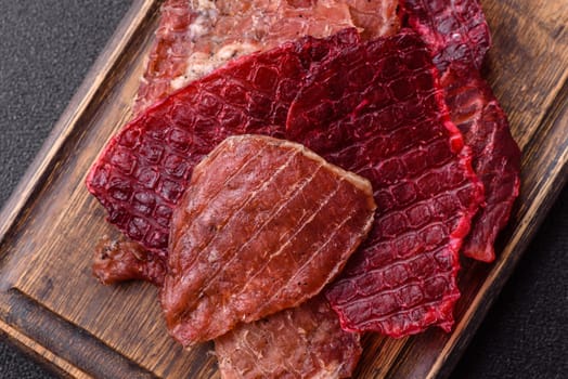Jerky, dried pork meat slices with salt and spices on a dark concrete background