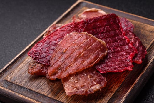 Jerky, dried pork meat slices with salt and spices on a dark concrete background
