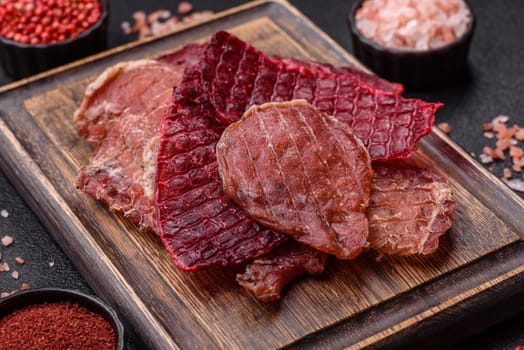 Jerky, dried pork meat slices with salt and spices on a dark concrete background