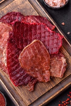 Jerky, dried pork meat slices with salt and spices on a dark concrete background