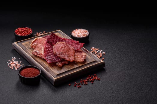 Jerky, dried pork meat slices with salt and spices on a dark concrete background
