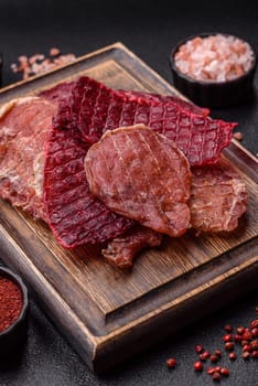 Jerky, dried pork meat slices with salt and spices on a dark concrete background