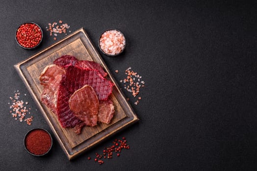 Jerky, dried pork meat slices with salt and spices on a dark concrete background