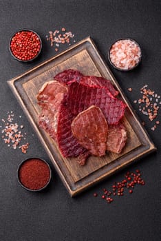 Jerky, dried pork meat slices with salt and spices on a dark concrete background