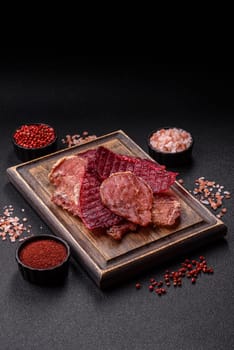 Jerky, dried pork meat slices with salt and spices on a dark concrete background
