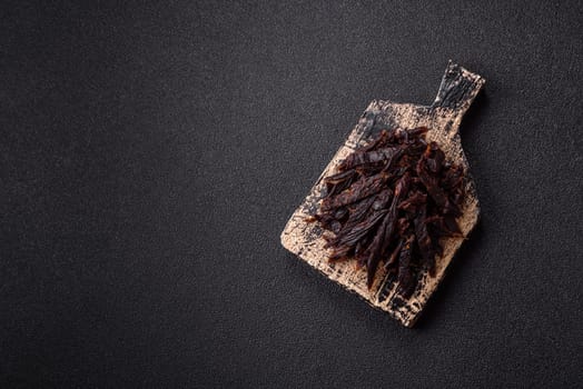 Jerky, dried horse meat or beef slices with salt and spices on a dark concrete background
