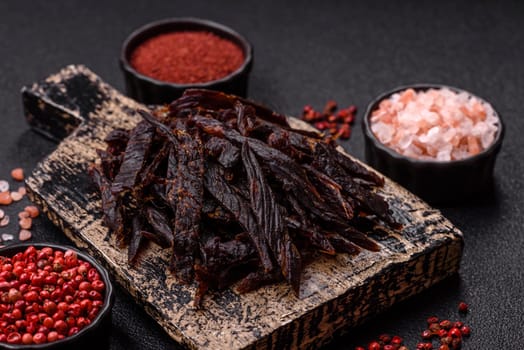Jerky, dried horse meat or beef slices with salt and spices on a dark concrete background