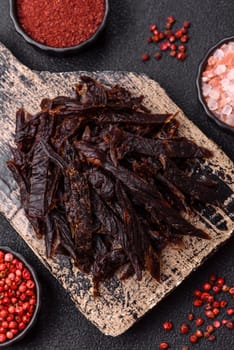 Jerky, dried horse meat or beef slices with salt and spices on a dark concrete background
