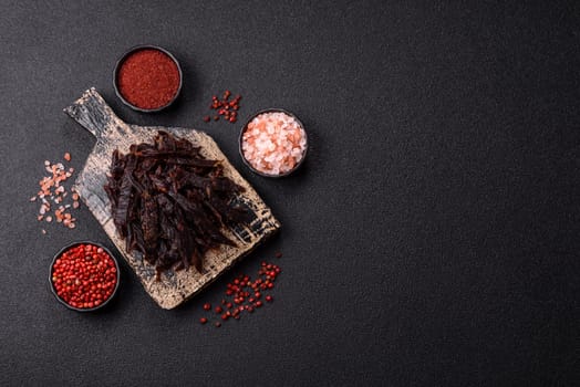 Jerky, dried horse meat or beef slices with salt and spices on a dark concrete background