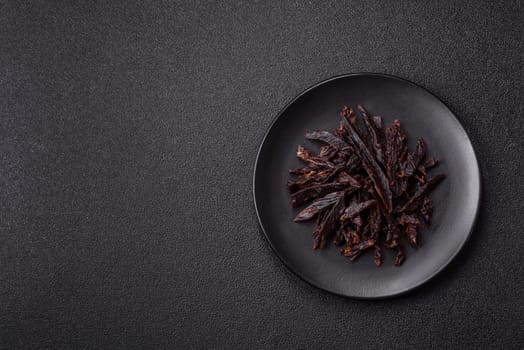 Jerky, dried horse meat or beef slices with salt and spices on a dark concrete background