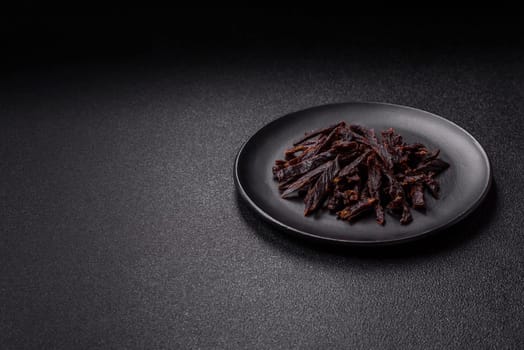 Jerky, dried horse meat or beef slices with salt and spices on a dark concrete background